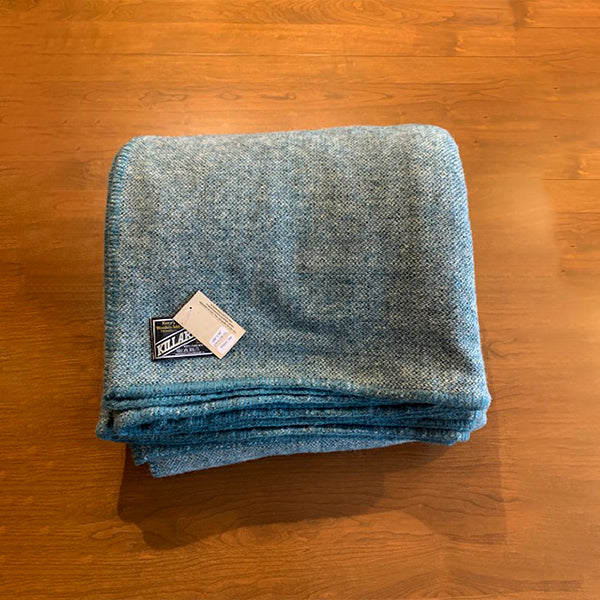 A photo of our extra large atlantic teal blanket against a rich cherry wood background.